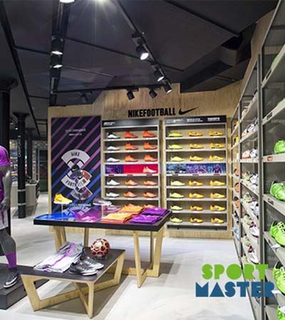View of Sportsmaster store with sport shoes on racks and two tables in the middle with sportswear with green and blue logo 